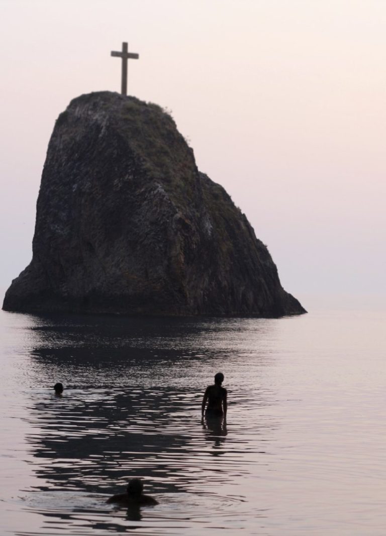 Silhouette von Menschen im Wasser vor einem Felsen mit einem Kreuz oben. Dies steht für die Discon GbR, Vertrauen und Ehrlichkeit.